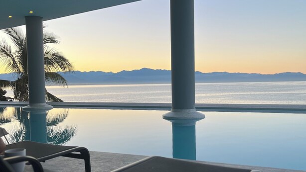 An infinity pool with a view of the sea and mountains, lounge chairs, and a table with a cup. - Spacious 3-brdm apartment near charming beach towns: security, bay access & gym (Bucerías)