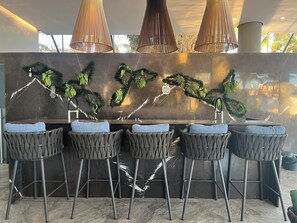 A modern bar area with a marble countertop, four bar stools, and decorative greenery.