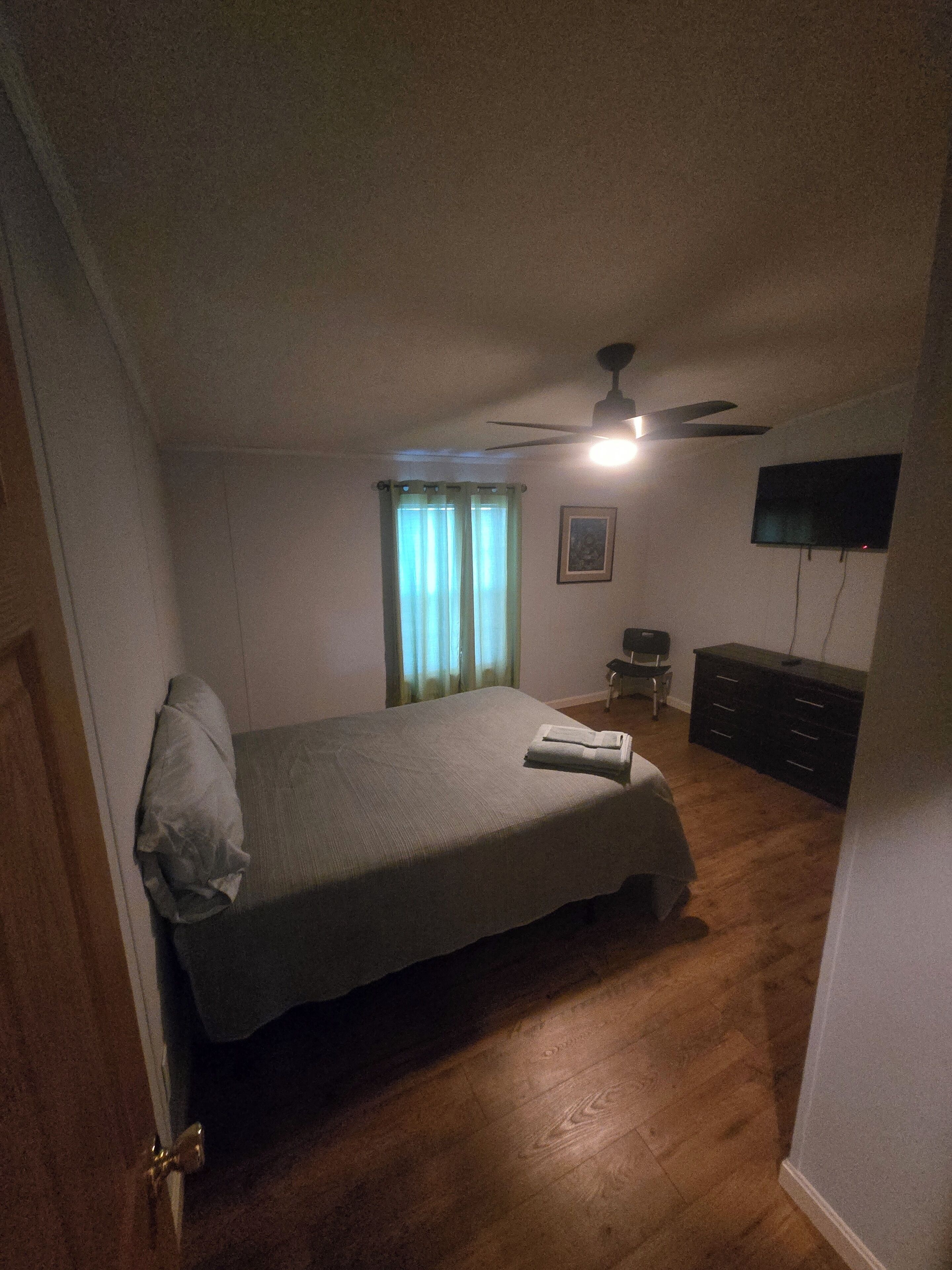 Ein Schlafzimmer mit einem Bett, einem Deckenventilator, einer Kommode und einem an der Wand befestigten Fernseher.