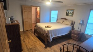 Un dormitorio con cama, ventilador de techo, escritorio, silla y ventana.