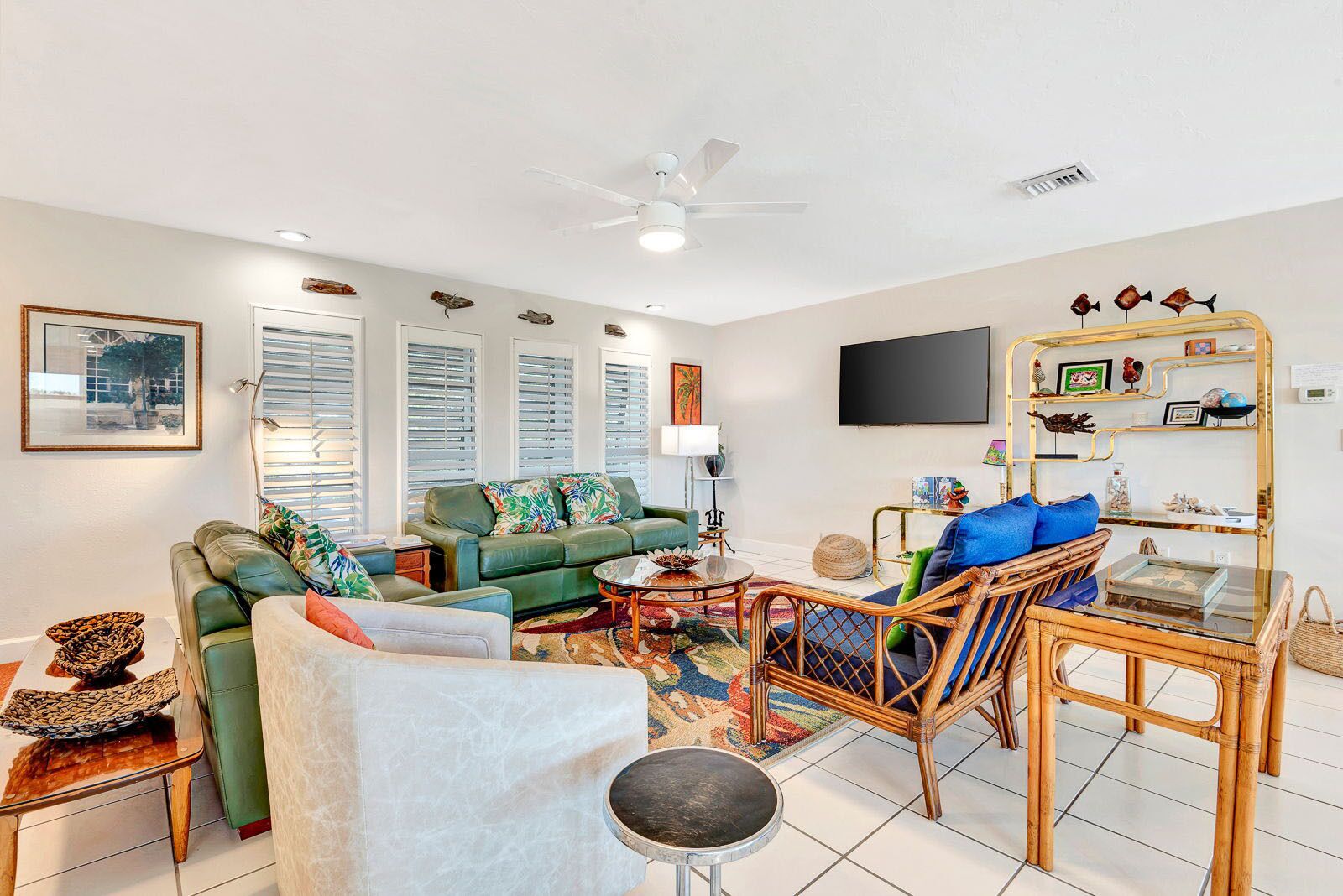 A living room with a green sofa, a wicker chair, a coffee table, and a TV mounted on the wall.