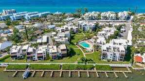 An aerial view of a coastal resort with modern buildings, a central swimming pool, and a marina with boats. - Tamarind 2BR – Pool, Boat Slips & Beach (Englewood)