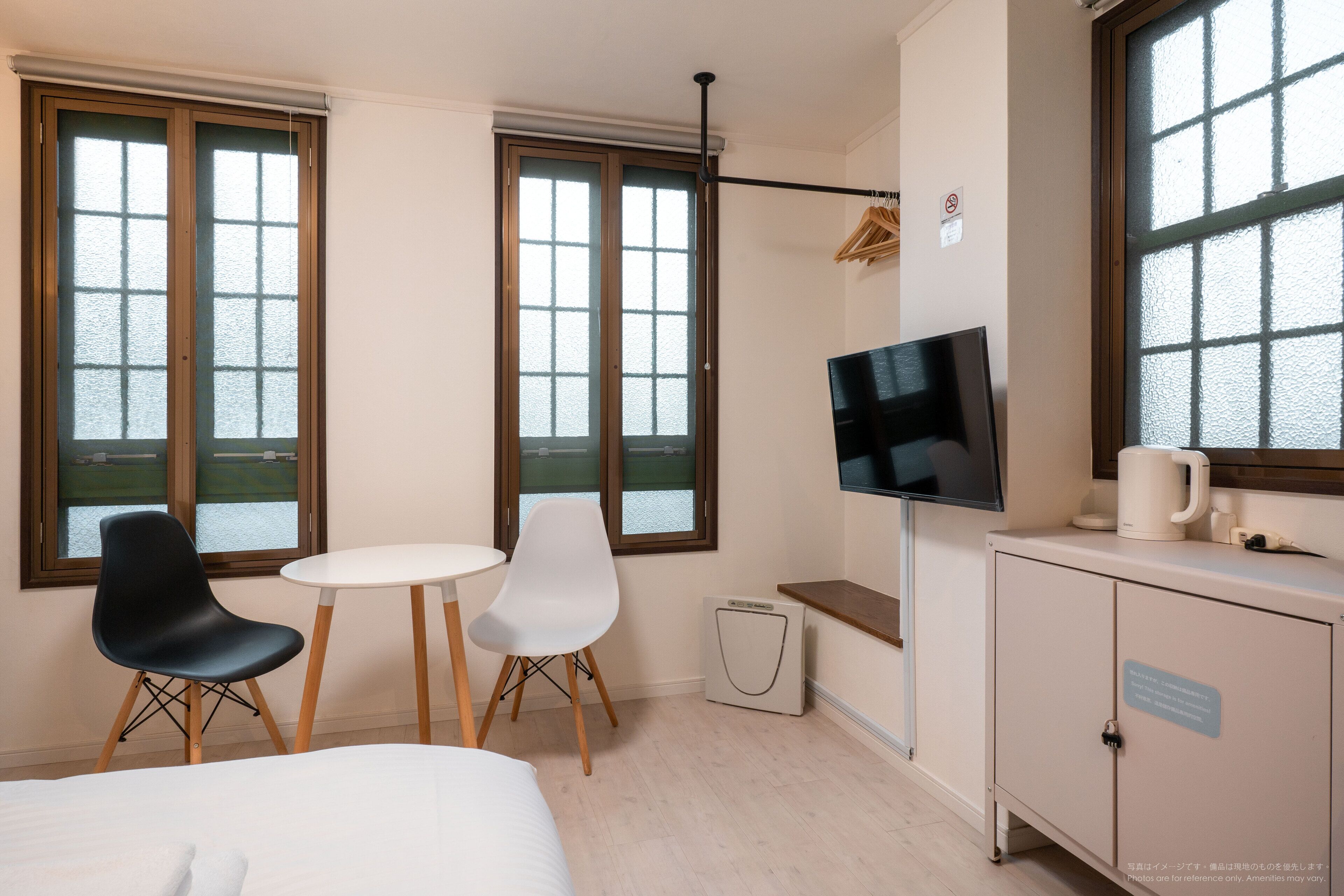 Habitación de hotel con una cama, dos sillas, una mesita, televisor, armario y ventanas amplias.