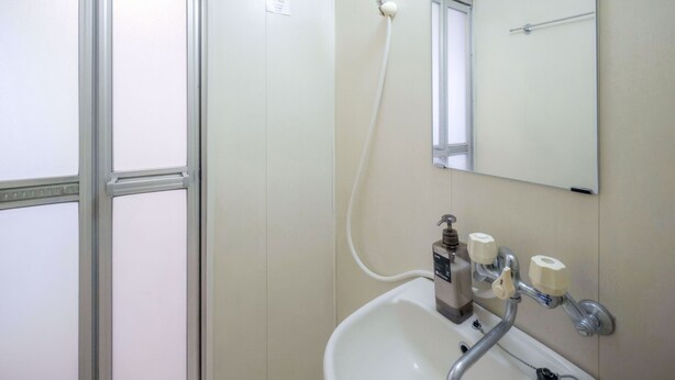 A bathroom with a white sink, a mirror, and a towel dispenser. - R Inn Nakano (Tokyo)