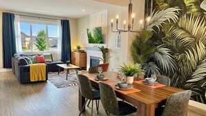 A modern living room with a sofa, dining table, chairs, and a large TV. - Family-Friendly Jungle Themed Home with Hot Tub, AC, and Tree Bunks. (Edmonton)