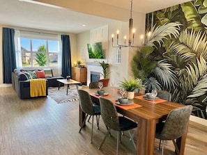 A modern living room with a sofa, dining table, chairs, and a large TV.