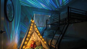 A room with a bunk bed, a tent with fairy lights, and a starry ceiling effect. - Family-Friendly Jungle Themed Home with Hot Tub, AC, and Tree Bunks. (Edmonton)