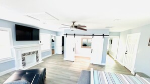 A spacious living room with a fireplace, a ceiling fan, and a large TV mounted on the wall.
