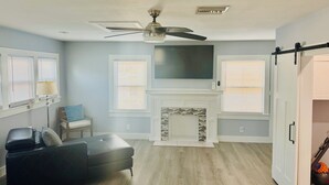 A living room with a fireplace, ceiling fan, and a large TV mounted above it.