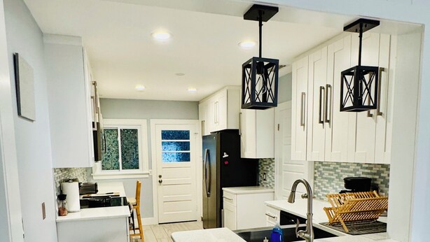 A modern kitchen with white cabinetry, a central island, and a black refrigerator.