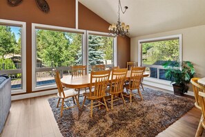 Un espace repas avec une table et des chaises en bois, de grandes fenêtres et un lustre.