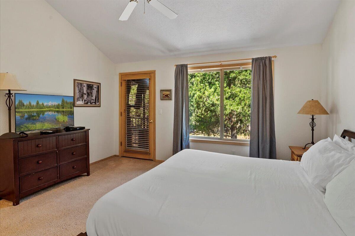 A bedroom with a bed, a dresser, a TV, a window with curtains, and a ceiling fan.