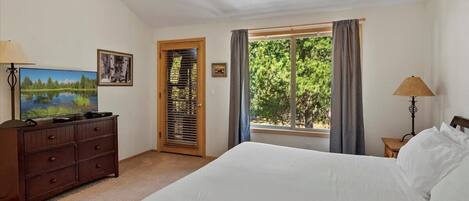 A bedroom with a bed, a dresser, a TV, a window with curtains, and a ceiling fan.