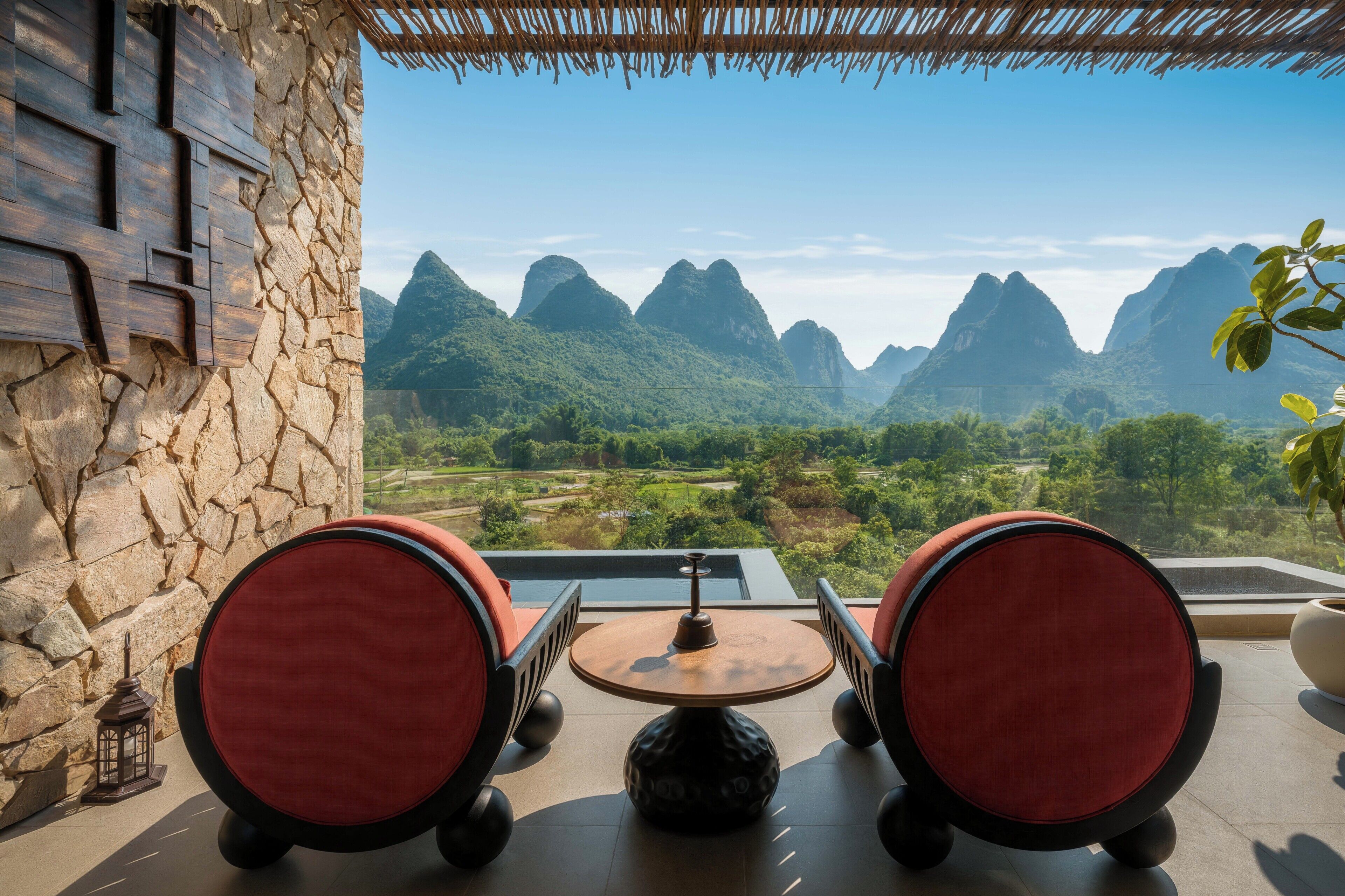 Una terraza con dos sillas rojas acolchadas y una mesita pequeña, con vistas a un paisaje montañoso.