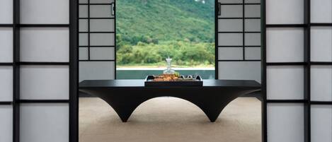 A room with a view of green mountains through a window, a black table with a tray of snacks, and a black chair.