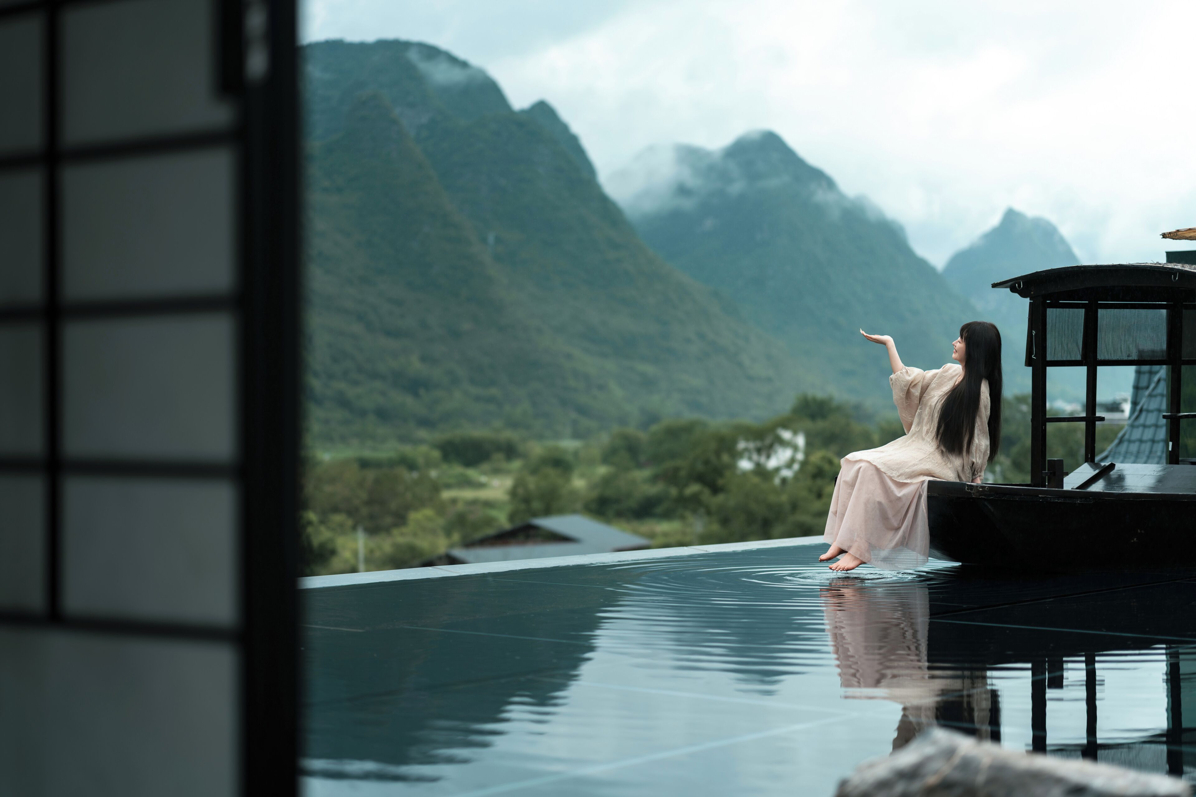 A person sitting on a reflective surface with a mountainous landscape in the background.