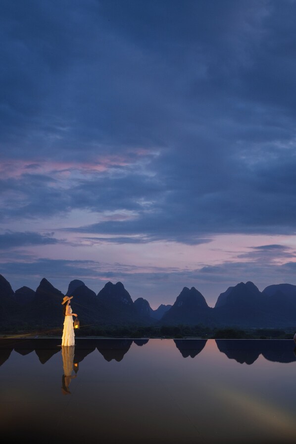 A calm lake with mountains in the background and a person standing by the water's edge. - The Deer Haven Yangshuo - A Luxury Heritage & Modern Karst Mountain Retreat by Yulong River (Guilin)