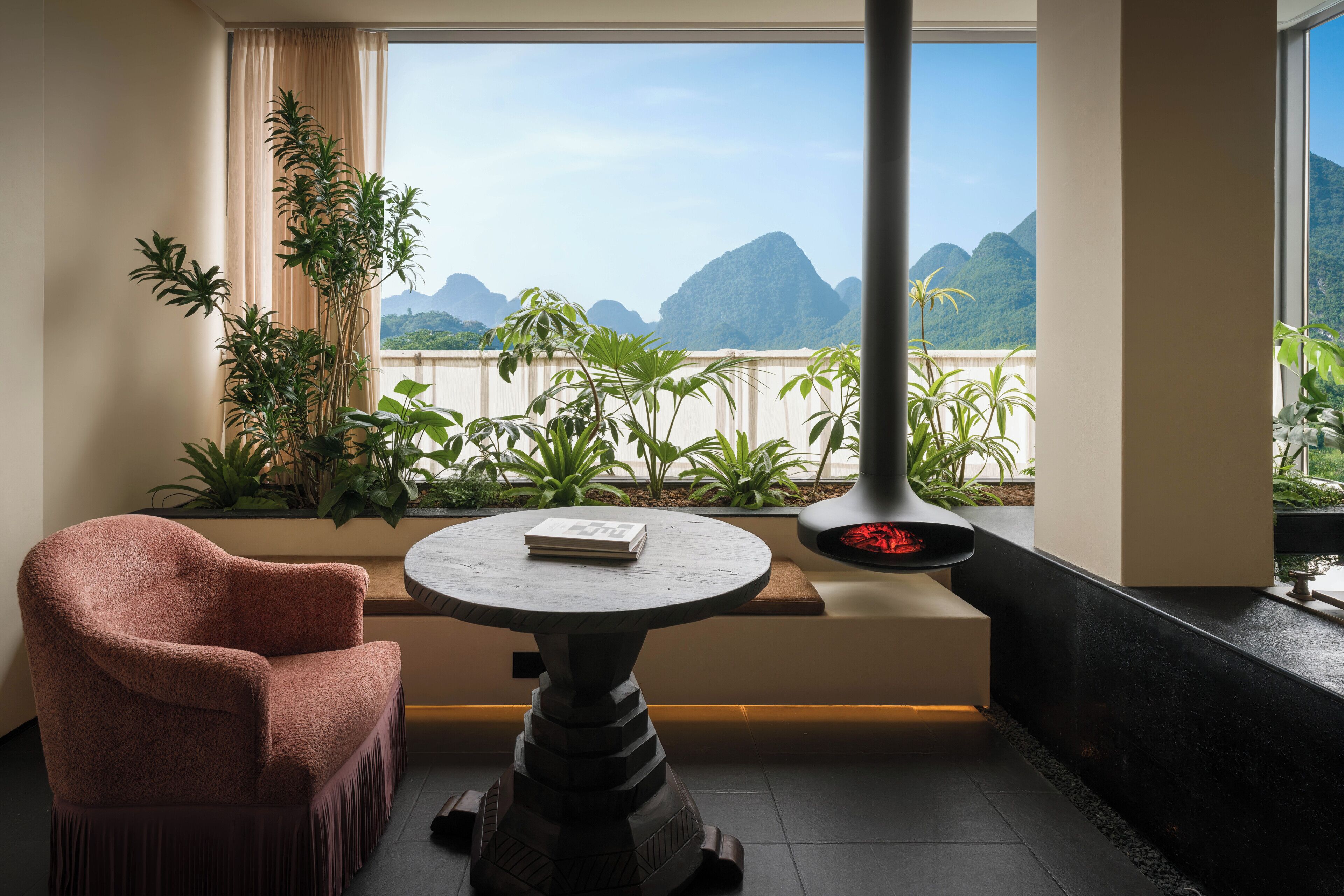 A room with a view of mountains, a table with a book, a chair, and a fireplace.