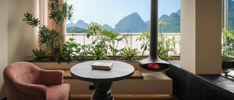 A room with a view of mountains, a table with a book, a chair, and a fireplace.