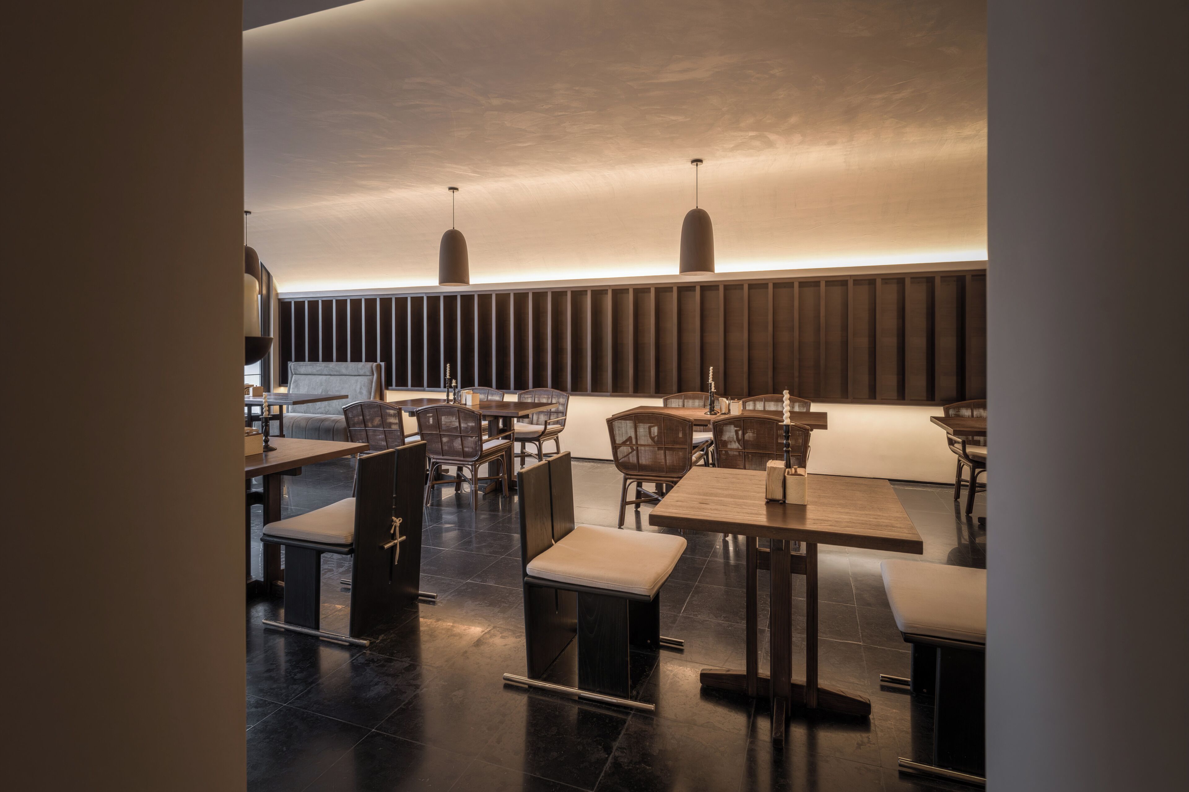 En modern restaurang med högt i tak, hängande lampor och en blandning av möbler i trä och stoppade möbler.