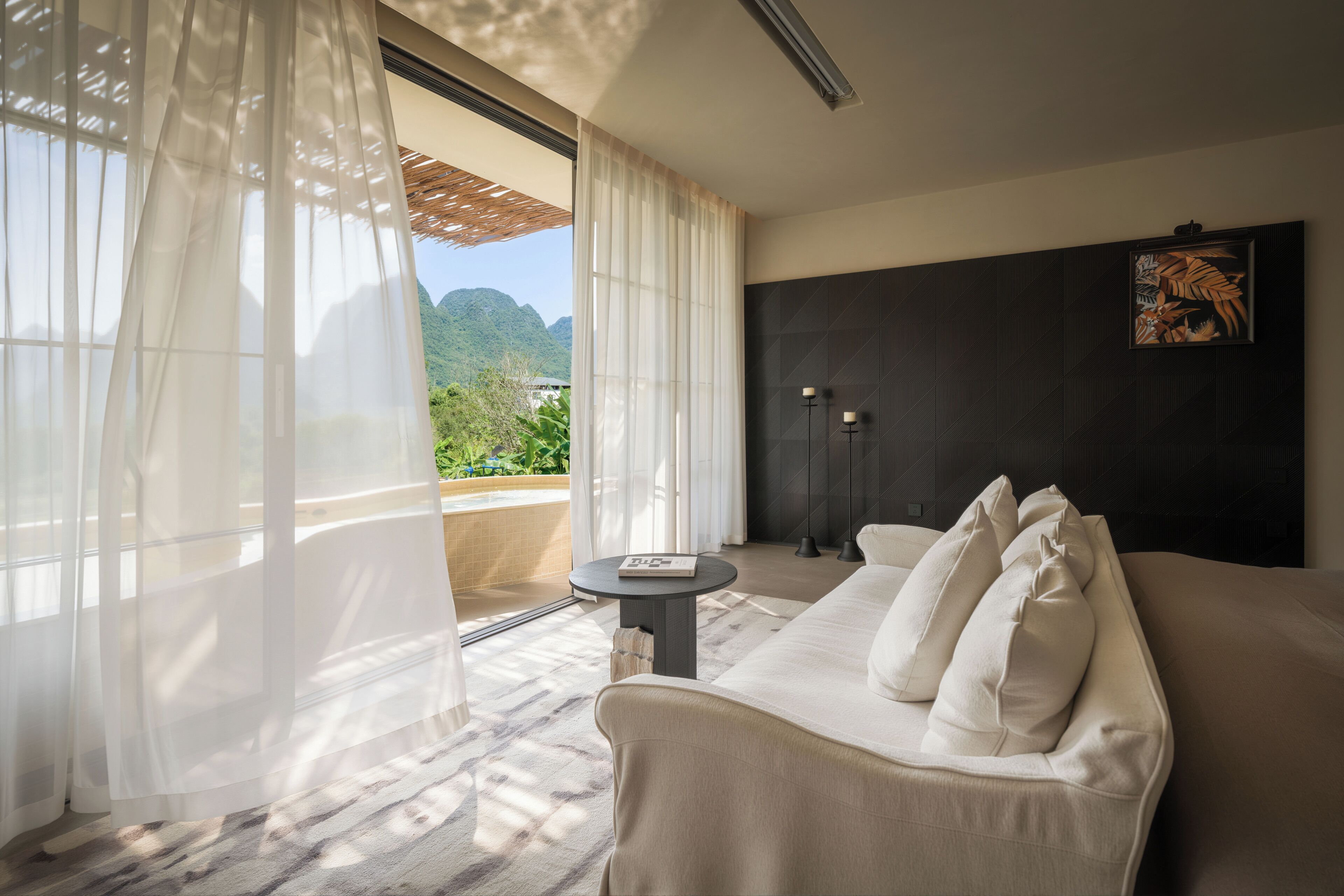 A modern hotel room with a sofa, a small table, and a view of a mountainous landscape.