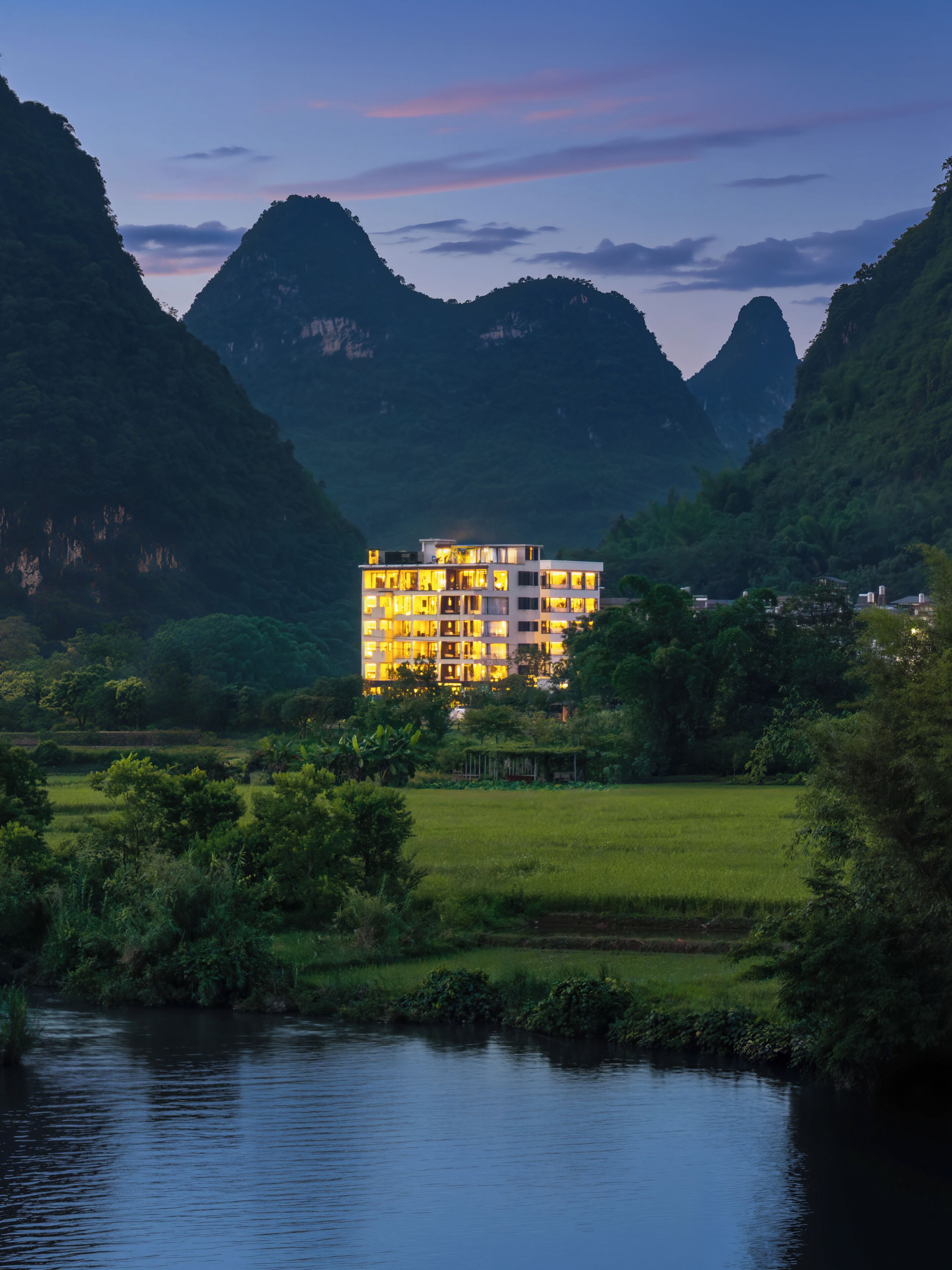 A multi-story hotel with a modern design, surrounded by lush greenery and mountains.