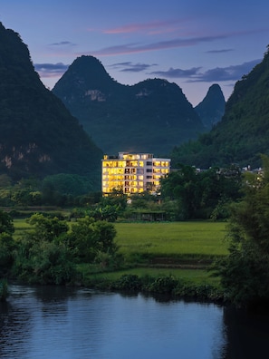 Un hôtel à plusieurs étages, doté d’un design moderne, entouré d’une végétation luxuriante et de montagnes.