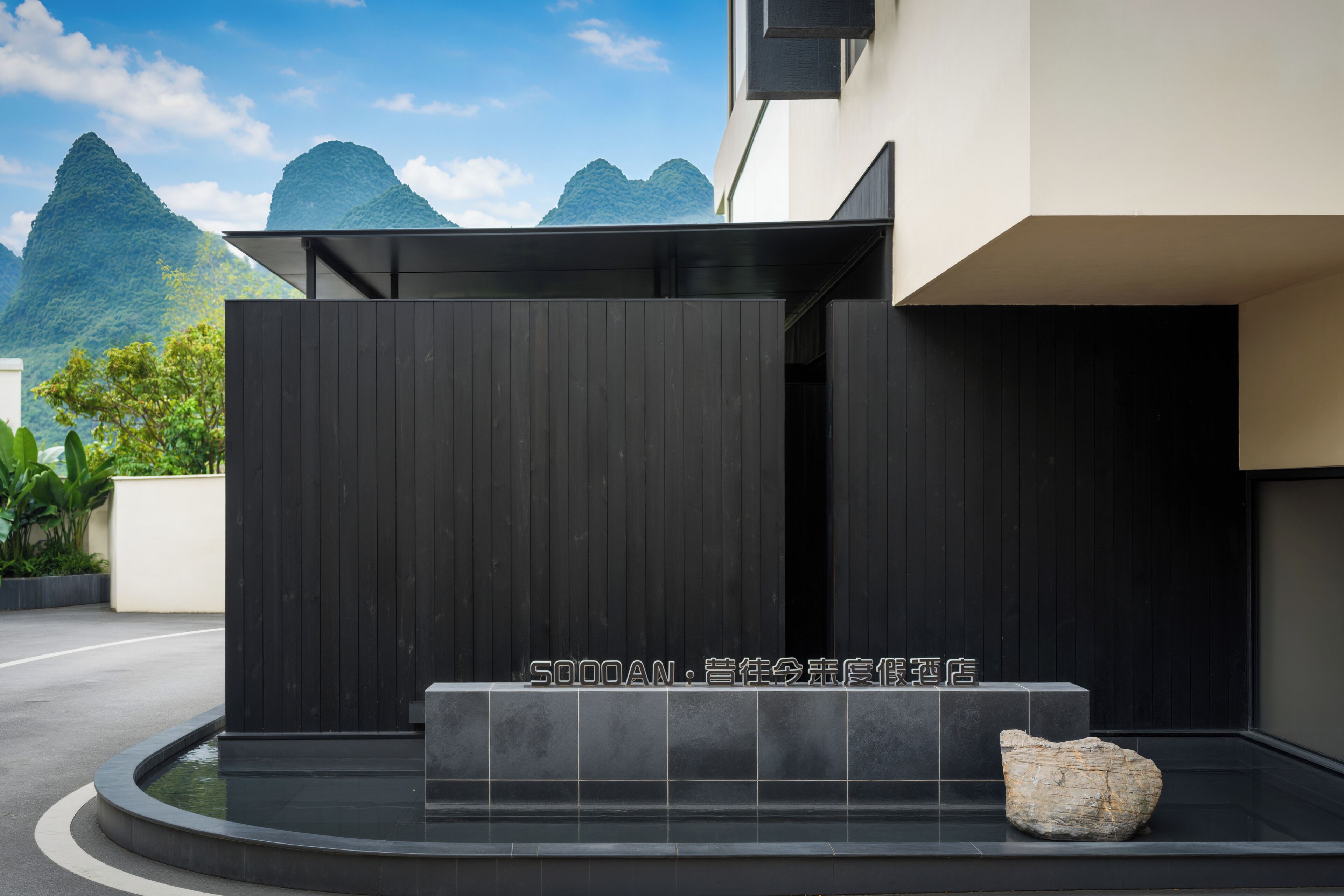 Un edificio moderno con fachada negra, una escultura de piedra y una vista despejada de montañas al fondo.
