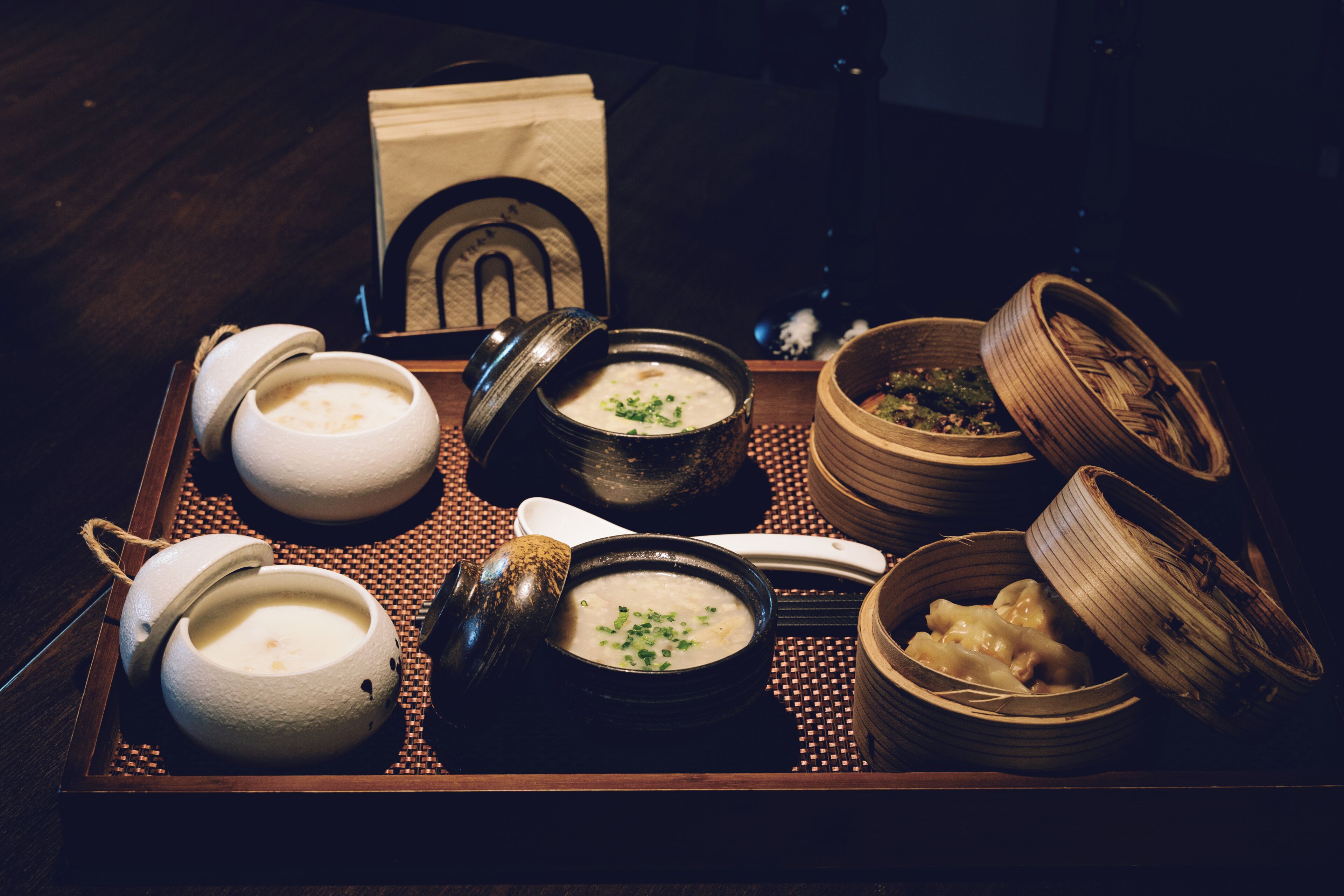 A tray with various bowls of food, including soup and dumplings, on a woven mat.