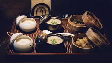 A tray with various bowls of food, including soup and dumplings, on a woven mat.