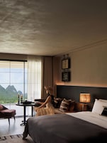 Habitación de hotel con una cama grande, una mesita de noche, una mesa con velas y vistas a montañas a través de amplios ventanales.