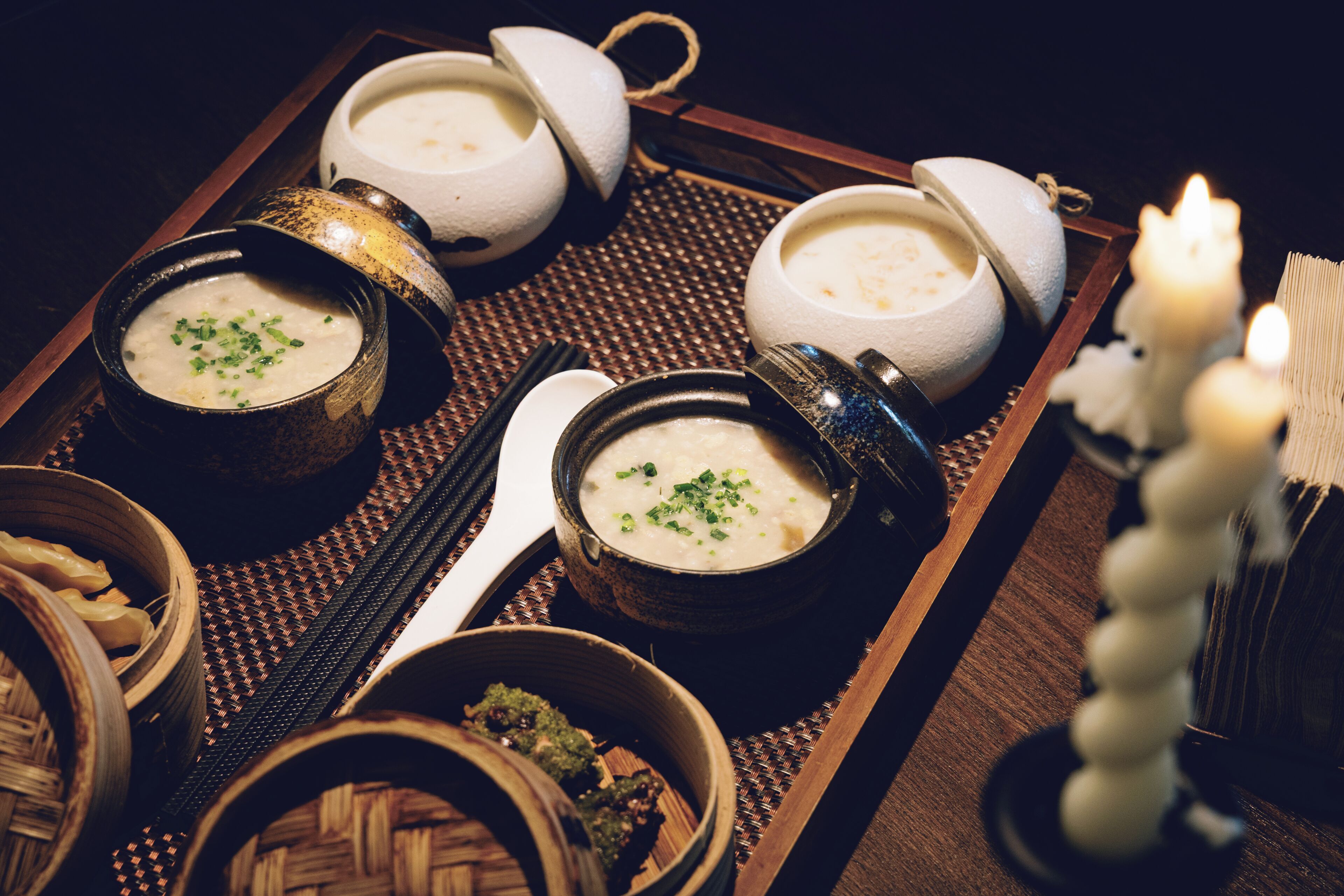 A tray with bowls of soup, a candle, and a traditional Japanese tea set.