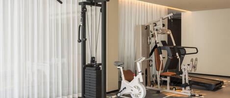 Une salle de sport équipée de matériel d’exercice, d’un vélo d’appartement et d’un téléviseur fixé au mur.