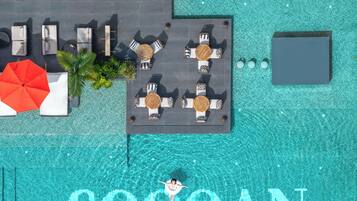 Vista aérea de una piscina con una persona flotando en el centro, rodeada de sillas y mesas de descanso.