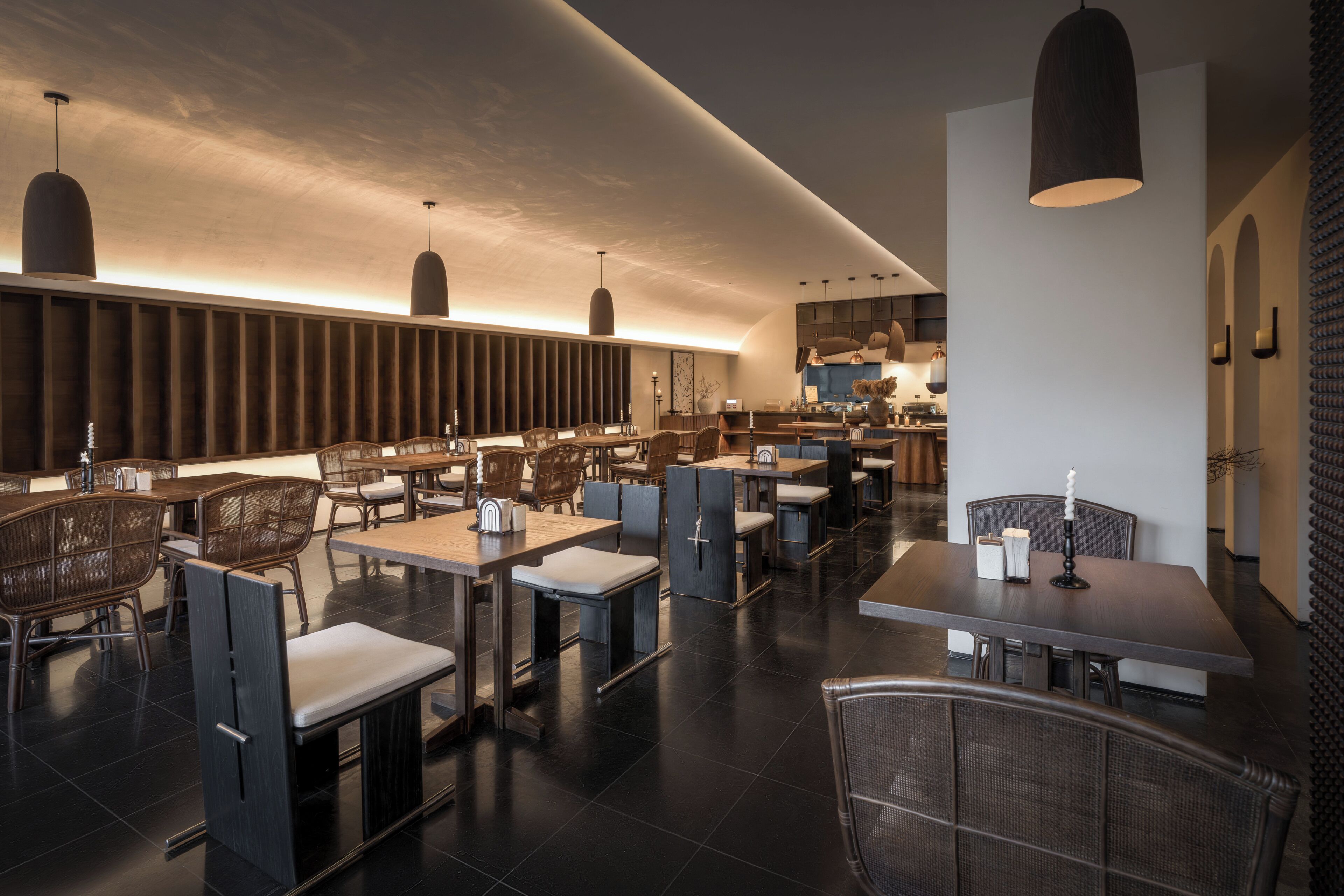 A modern restaurant interior with high tables and chairs, pendant lighting, and a visible kitchen area.