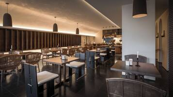 A modern restaurant interior with high tables and chairs, pendant lighting, and a visible kitchen area.