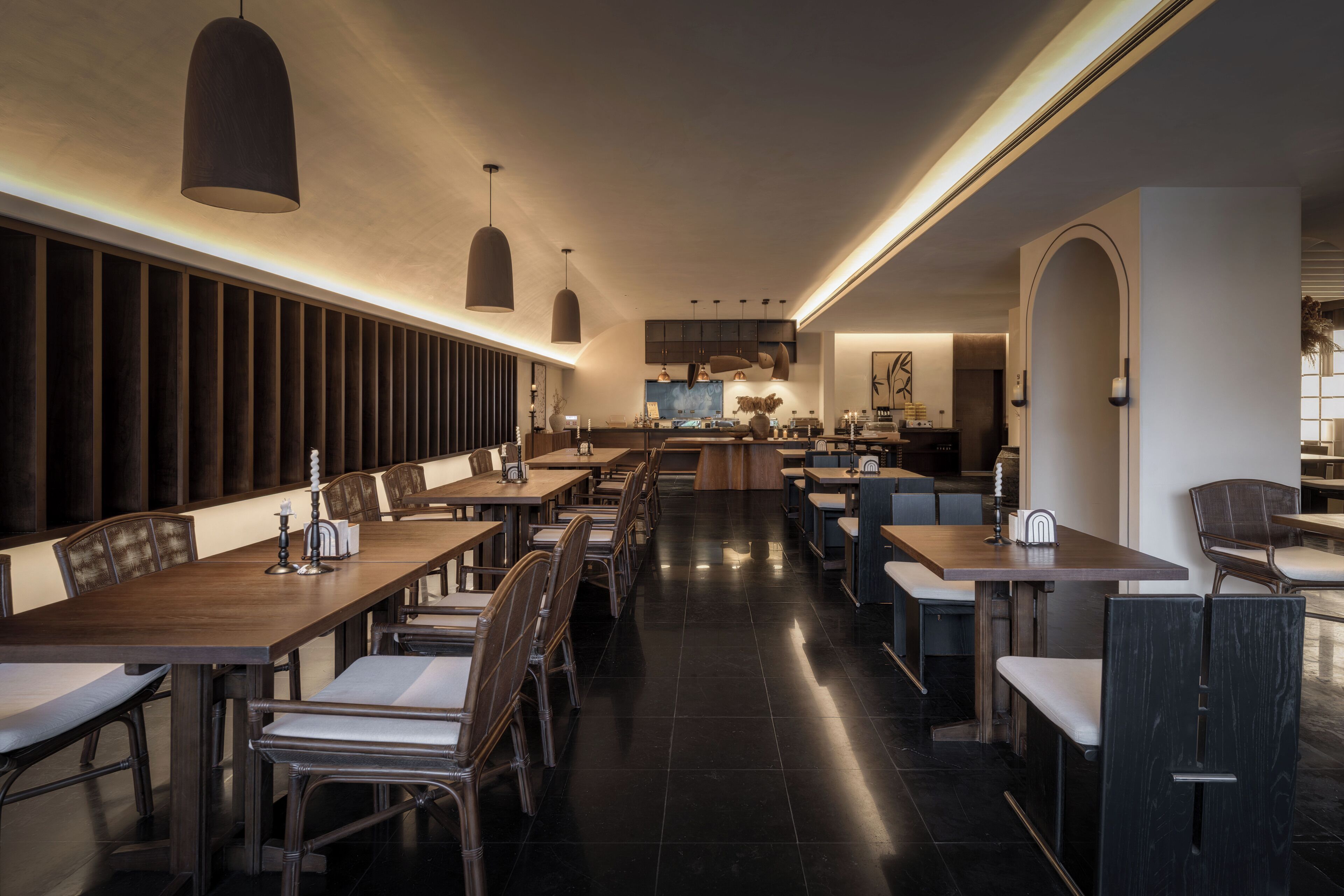 A modern restaurant interior with long communal tables and individual booths, a kitchen in the background, and a clean, minimalist design.