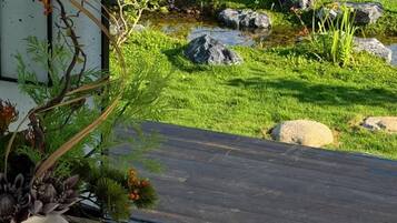 A wooden deck with a tray of food items, a white vase with plants, and a view of a well-maintained garden with rocks and grass.