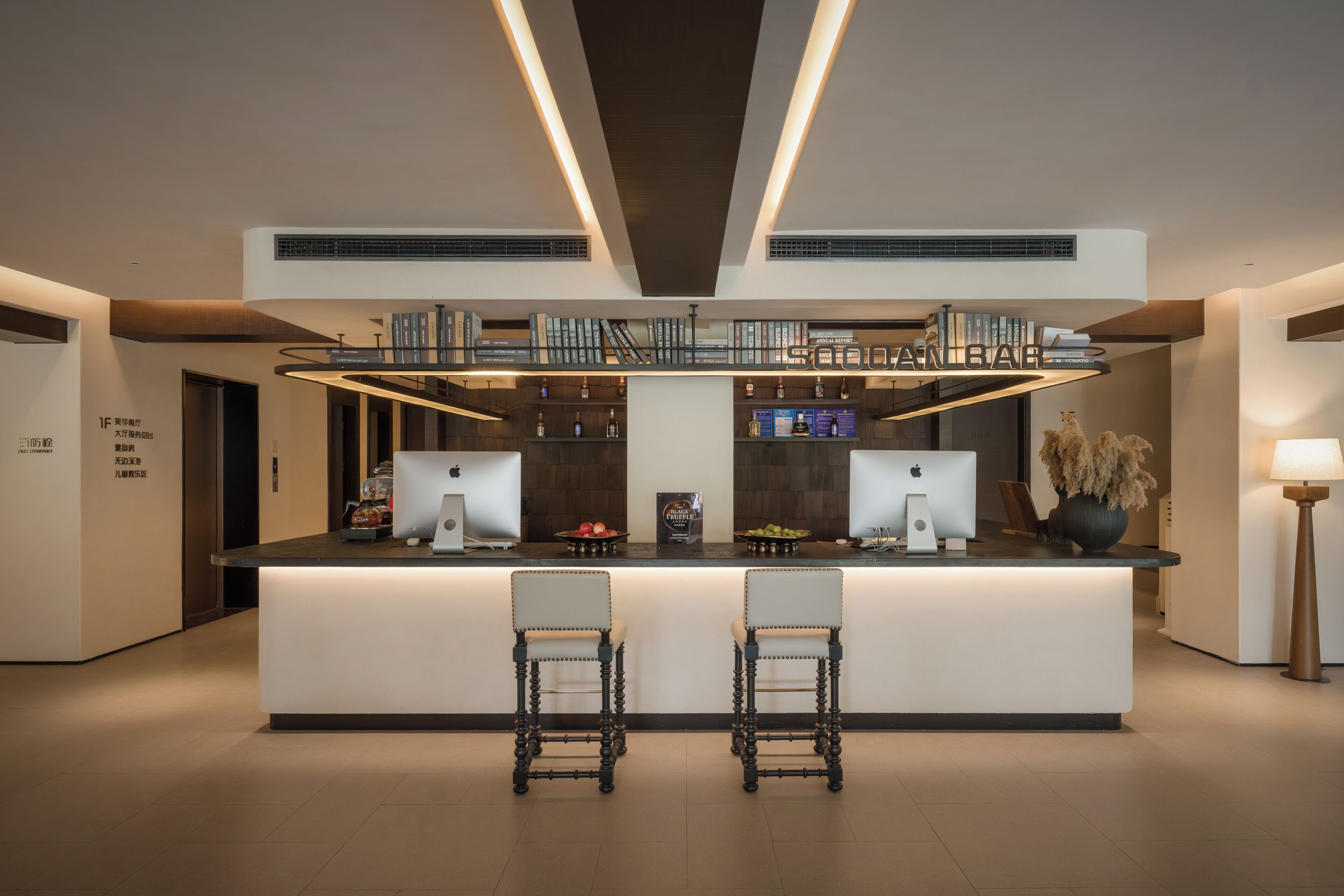 A modern bar area with two bar stools, a central counter, and a bookshelf with books and bottles.