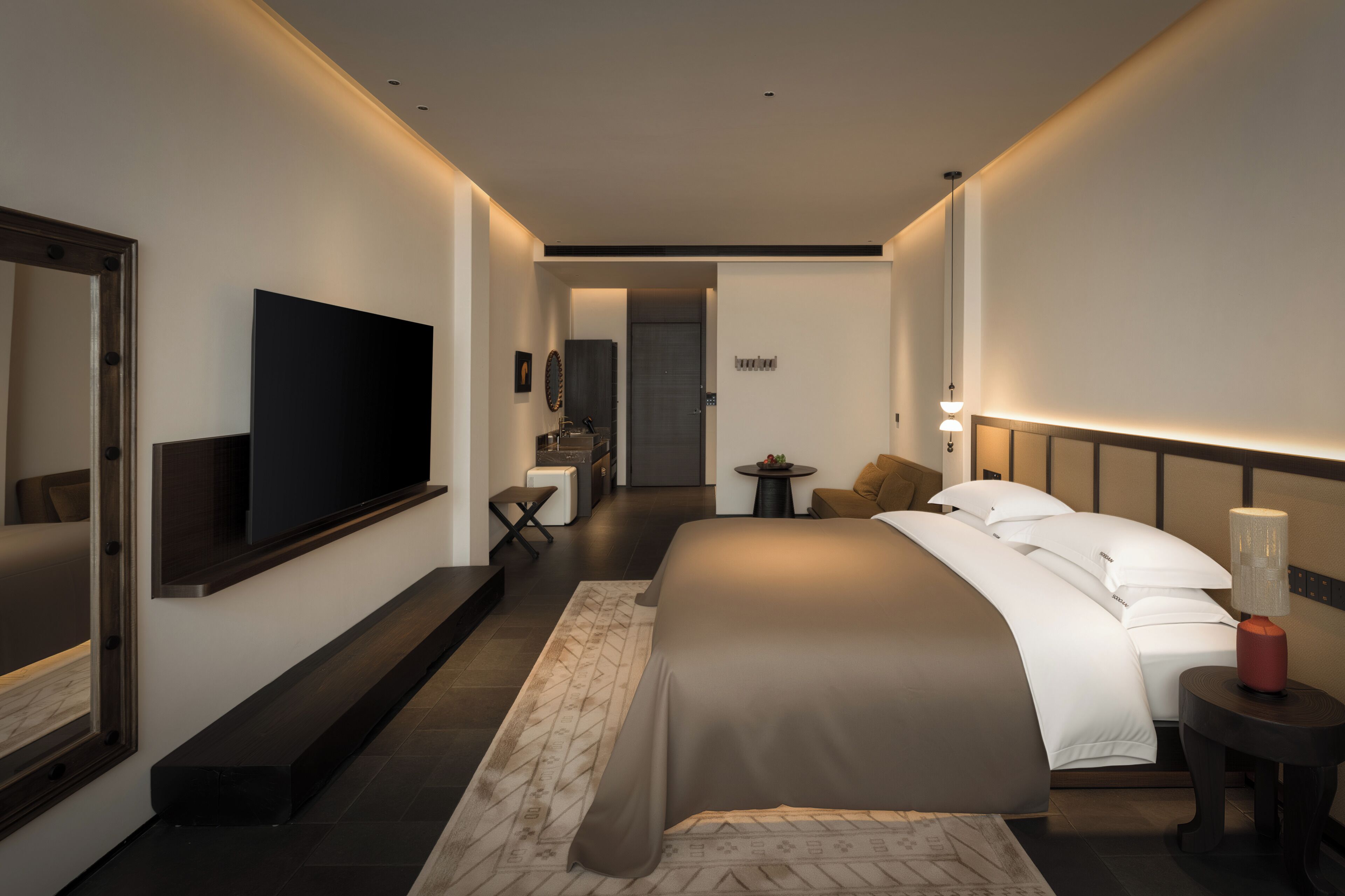 A modern hotel room with a large bed, a flat-screen TV, a desk, and a mirror.