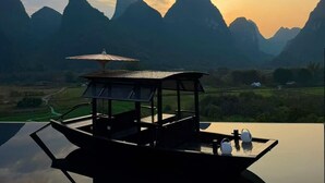 A wooden structure with a roof and a table, surrounded by a reflective water surface, set against a mountainous landscape during sunset. - The Deer Haven Yangshuo - A Luxury Heritage & Modern Karst Mountain Retreat by Yulong River (Guilin)