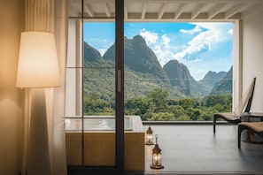 Une pièce avec une grande fenêtre, une chaise, une table et une lampe.