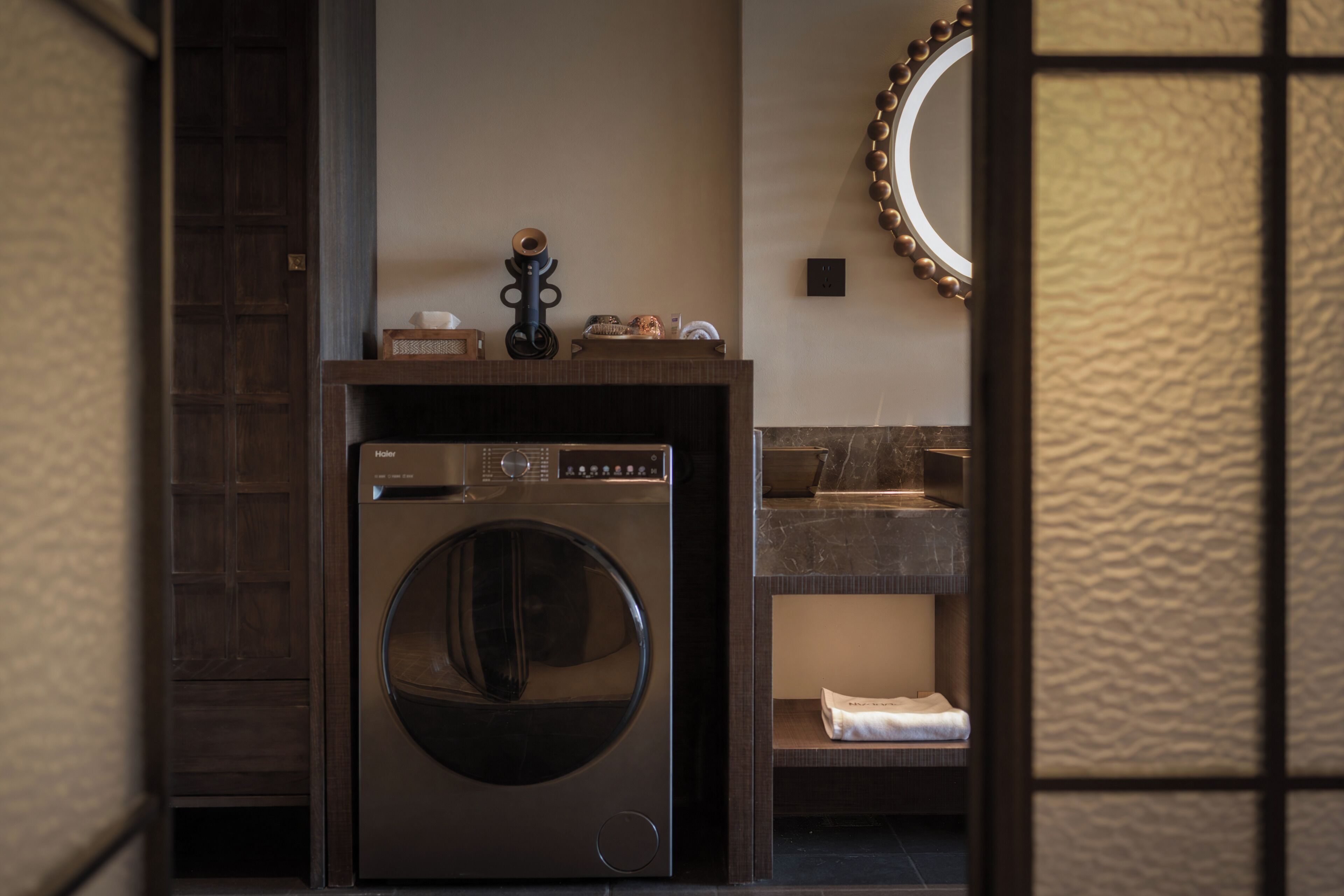 Un baño moderno con lavadora y secadora integradas, un tocador de madera y un espejo con marco decorativo.