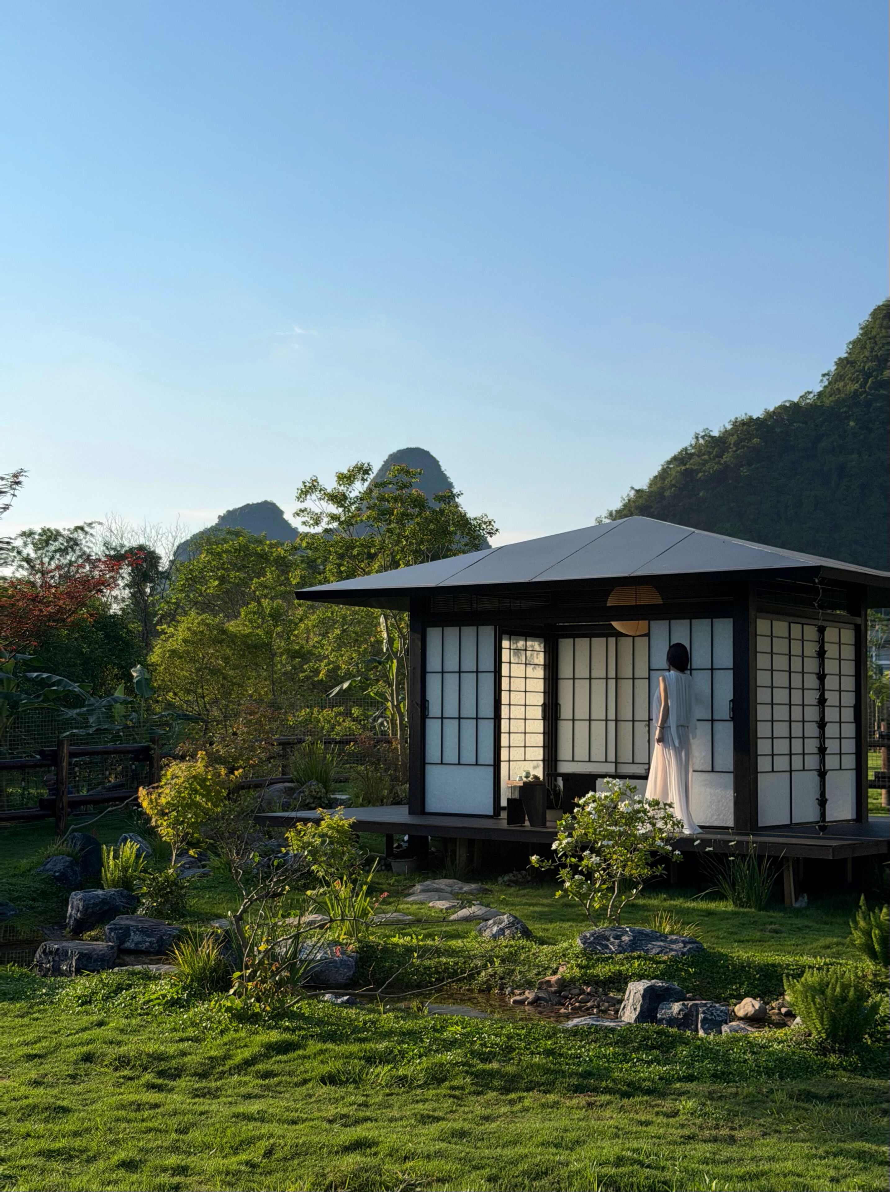 Un edificio de estilo japonés tradicional con suelo de esteras de tatami, rodeado por un jardín cuidado con rocas y plantas.
