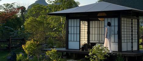Un edificio de estilo japonés tradicional con suelo de esteras de tatami, rodeado por un jardín cuidado con rocas y plantas.