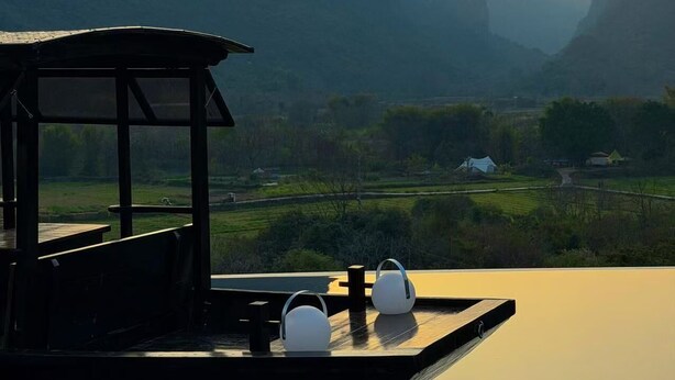 A terrace with a view of mountains at sunset, a table, and two white spherical objects. - The Deer Haven Yangshuo - A Luxury Heritage & Modern Karst Mountain Retreat by Yulong River (Guilin)