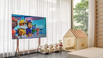 A living room with a flat-screen TV, a wooden playhouse, and a window with sheer curtains.