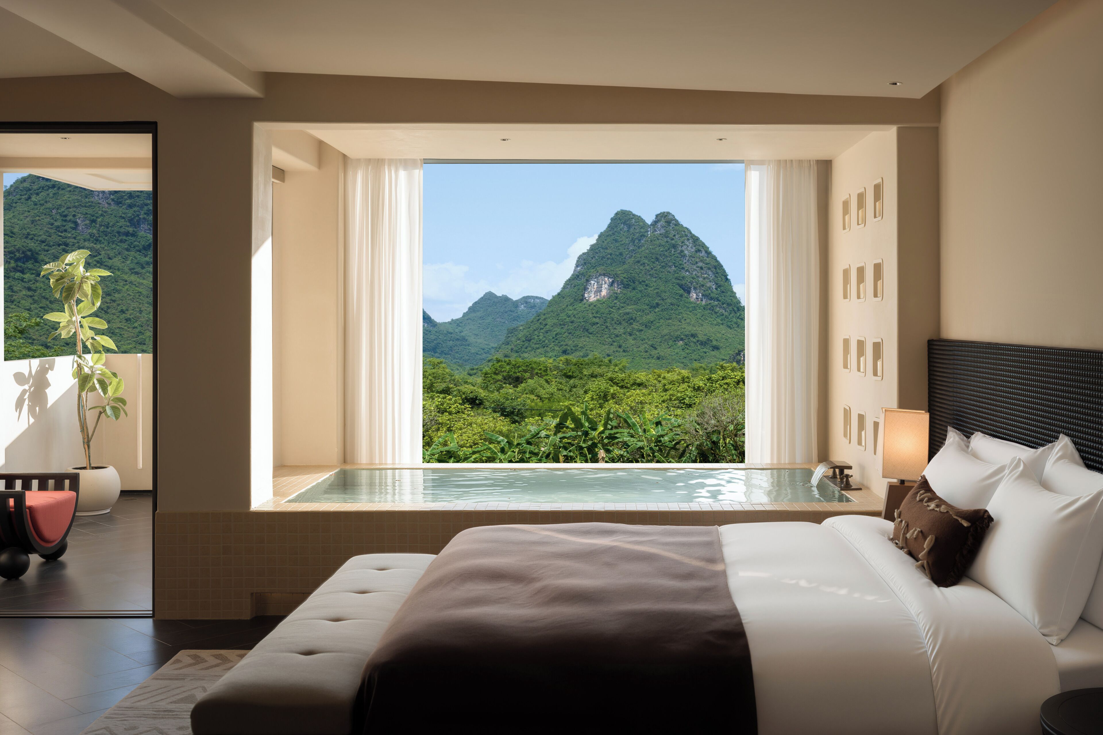A bedroom with a large bed, a view of mountains, and a small pool.