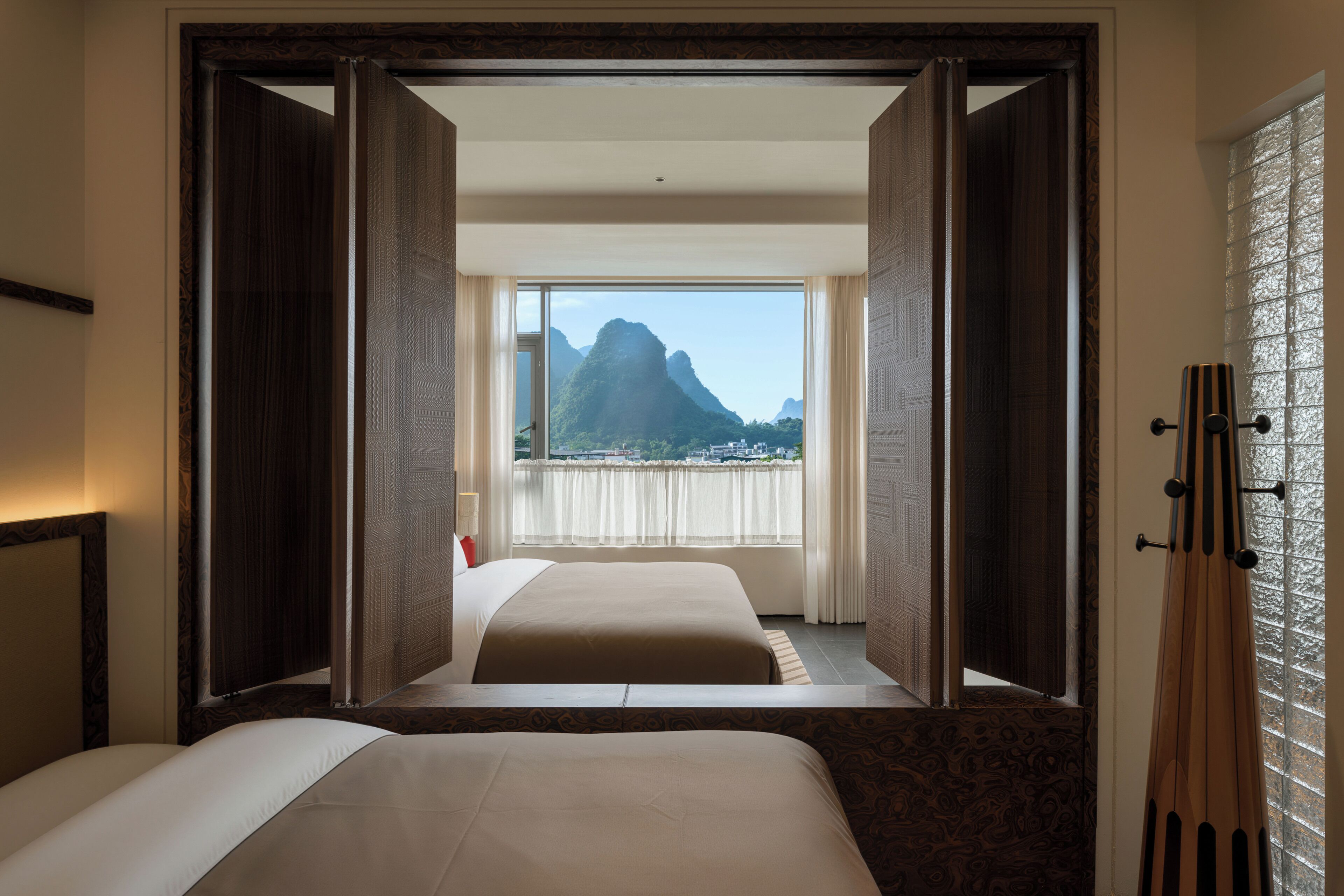 Ein Hotelzimmer mit Bett, einem Fenster mit Vorhängen und Blick auf Berge.