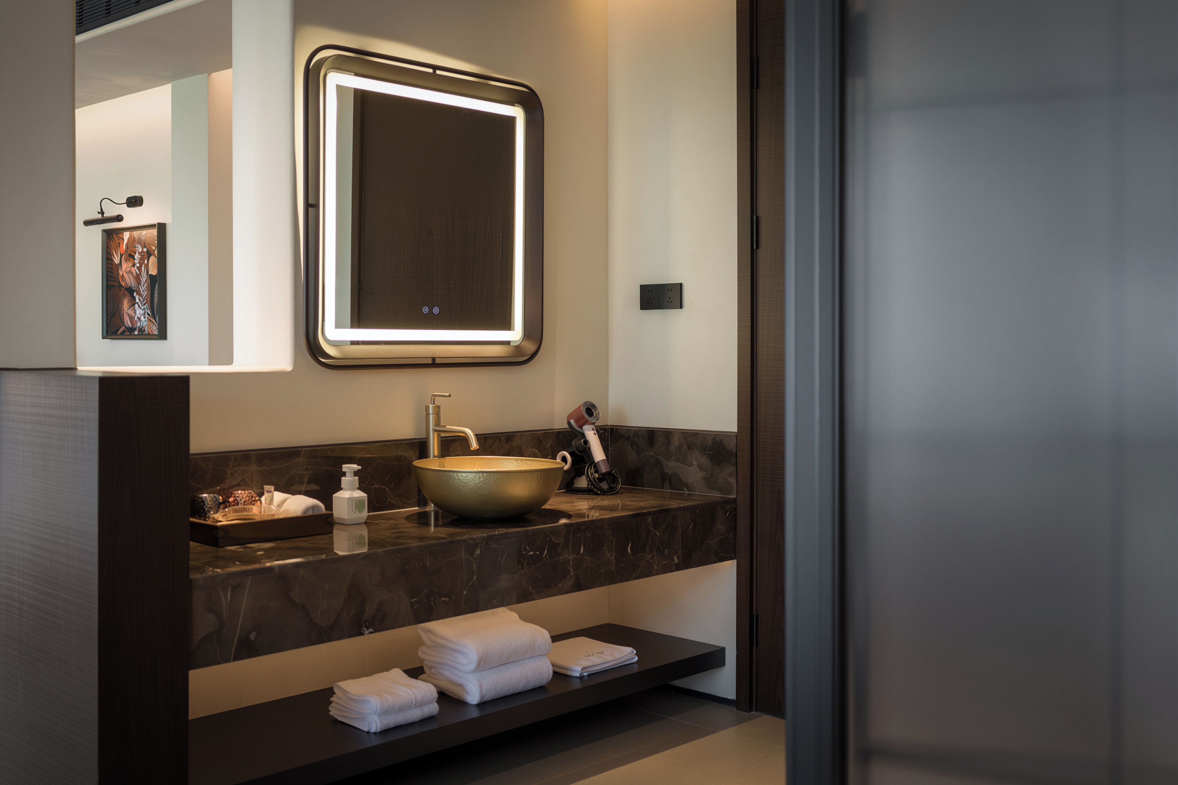 Un baño moderno con un espejo grande, un lavabo sobre encimera y una superficie con artículos de aseo.